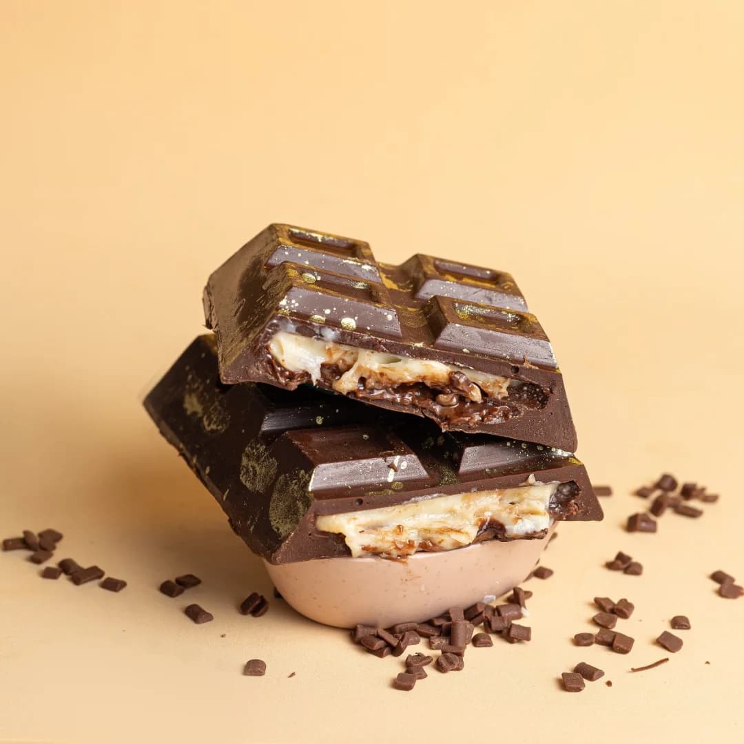 Duas barras de chocolate recheadas, partidas e empilhadas, mostrando o recheio cremoso
