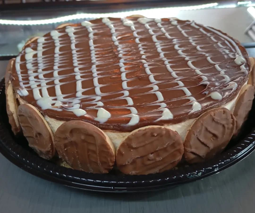 Torta inteira com cobertura escura e brilhante, fios brancos por cima e biscoitos redondos em volta